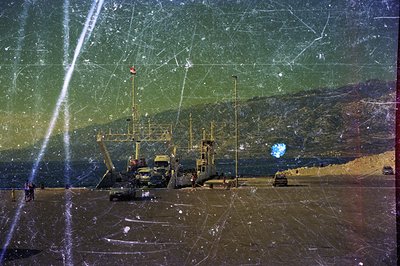 Seaside scene features a landing craft carrier and personnel unloading cargo. The coastal landscape includes a beach, vehicle...