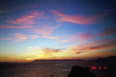Dramatic twilight seascape with vibrant pink and orange clouds reflecting on still water. Distant landmasses silhouette the h...
