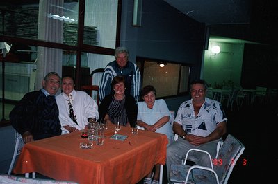 Group portrait of six adults seated around an orange-covered table, likely in a restaurant or resort setting. Visible glasswa...