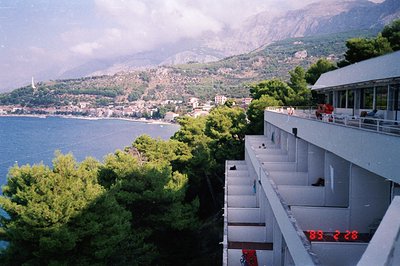 Seaside resort architecture, likely 1970s, overlooking a coastal town nestled between mountains and the Adriatic Sea. Concret...