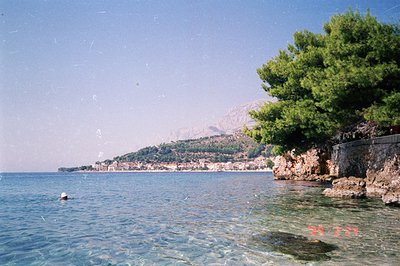 Seaside view of a coastal town, possibly Bulgaria or Romania, with clear turquoise waters and a mountainous backdrop. A lone ...