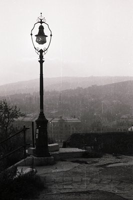 A wrought iron lamppost stands prominently on a stone ledge overlooking a city panorama, likely a European coastal town. The ...