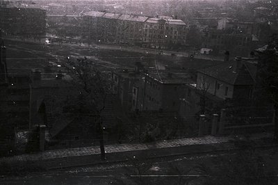 High-angle, grayscale view of a residential neighborhood, likely post-war era. Buildings feature steep roofs and varied archi...