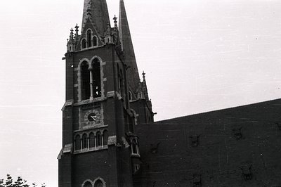 Ornate, dark brick church tower with pointed spire and clock face. Gothic Revival architecture featuring detailed tracery and...