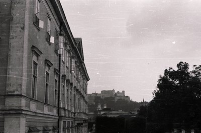 Striking black and white image captures a grand building facade with symmetrical windows and ornate detailing. A distant cast...