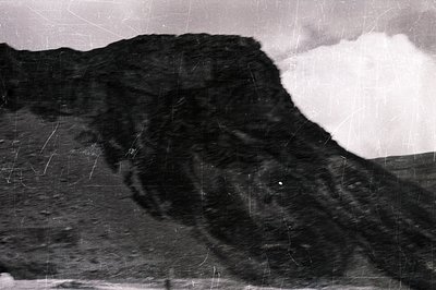 Striking black and white photo featuring a dramatic, rocky cliff face under a cloudy sky. Texture and erosion are evident on ...