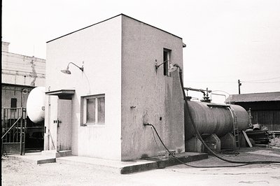 Industrial complex with a monolithic concrete structure, featuring a large propane tank and connected piping system. The buil...