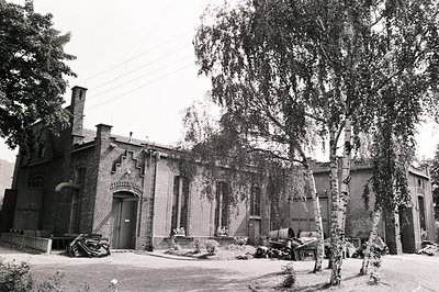 Classic industrial brick building featuring arched entrances & a prominent chimney. Visible machinery and equipment suggest a...