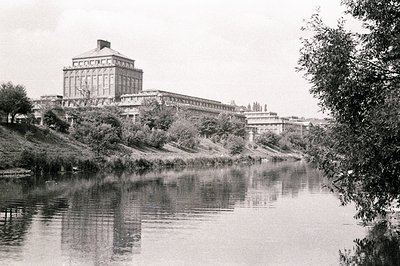 A monumental, classically-inspired building dominates the view, reflected in a still river. Extensive stonework, symmetrical ...