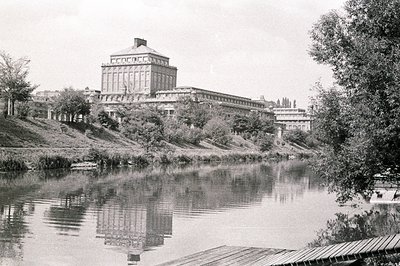 A grand, symmetrical building with a central tower dominates the view, reflected in the still waters of a lake. Architectural...