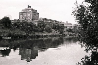 Grand, imposing building with a central tower, reflecting in still water. Classic architectural style, possibly civic or inst...