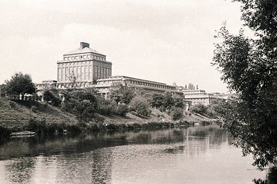 Grand, imposing institutional building with classical details rises above a riverbank. Multi-story structure features a promi...