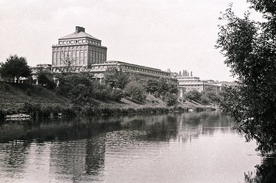 A grand, neoclassical building with a central cupola dominates the scene, situated on a raised bank overlooking a wide river ...