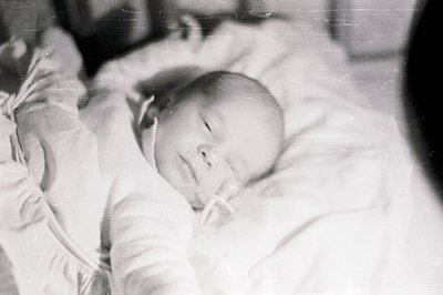Close-up, monochrome portrait of a peacefully sleeping infant swaddled in soft fabric. The image exhibits characteristic grai...