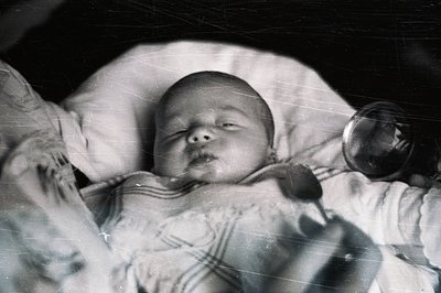 A monochrome portrait shows a peacefully sleeping baby swaddled in a striped blanket. The image exhibits visible grain and sc...