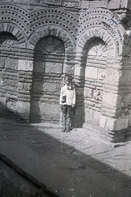 A young boy stands beneath a series of arched stone openings. The structure’s exterior features detailed relief carvings arou...