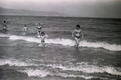 A candid moment capturing a family enjoying a day at the beach. Several figures wade into the breaking waves, a young boy in ...