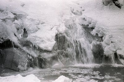 Frozen waterfall cascades over ice-encrusted rock formations. Ice structures cling to the rock face, exhibiting intricate pat...