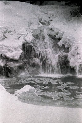 A frozen waterfall cascades over ice formations in a dramatic, monochrome landscape. Water droplets hang suspended, captured ...