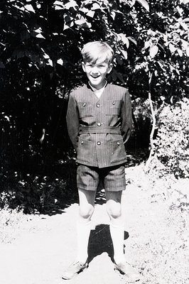 Young boy in a tailored double-breasted jacket & shorts, knee socks, stands outdoors. Appears to be a formal school or unifor...