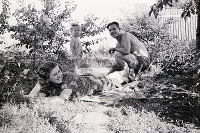 A 1960s family portrait captures a relaxed moment outdoors. A woman reclines on a blanket, a man kneels nearby, and a young c...