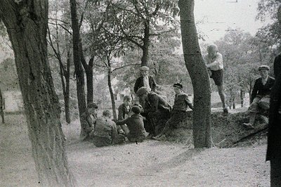 Group of young boys in military-style uniforms gathered around a raised earthen mound in a wooded area. Likely a scout troop ...