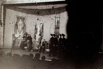 Formal ceremony depicted indoors, featuring military personnel near draped flags and a statue. Appears to be a graduation or ...