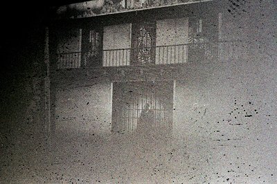 Monochromatic image showcasing a building facade with multiple windows, featuring a balcony detail. The grainy quality sugges...