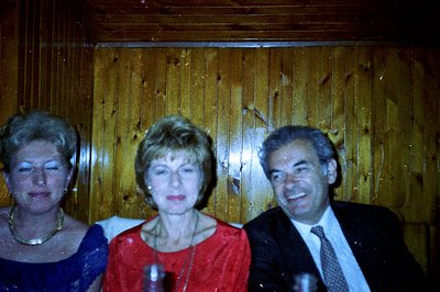 Three individuals posing for a photograph against a wood-paneled backdrop. Two women wear formal attire; one in blue, the oth...