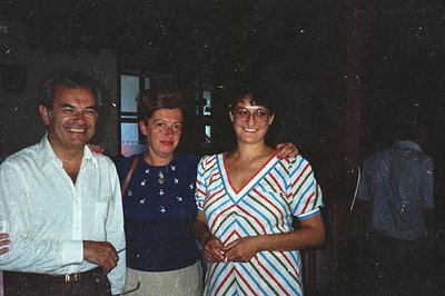 Three individuals pose closely in a casual setting. The man on the left wears a linen shirt, the woman in the center, a patte...