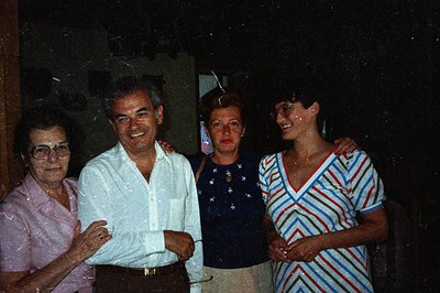 Four individuals pose for a candid snapshot. The subjects wear 1970s-era attire: a pink shirt, a white collared shirt, a patt...