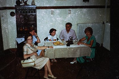 A candid, slightly grainy photograph captures a family gathered around a table laden with fruit, likely lemons. Four individu...