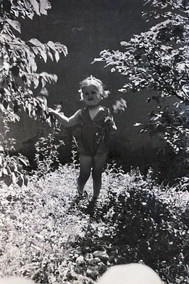 A young girl in a patterned romper playfully runs through foliage, arms outstretched. The image captures a moment of childhoo...