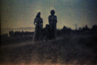 Dusty, faded photographic print shows two figures and a child silhouetted against a distant, hazy landscape. The visible grai...
