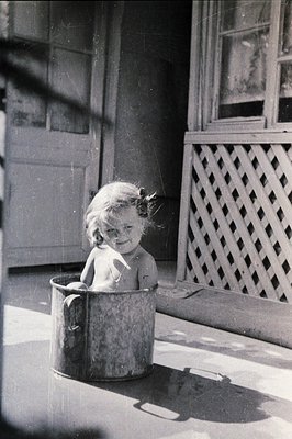 A young child, likely a toddler, sits happily inside a metal bucket. The image appears to be taken outdoors, potentially on a...