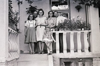 Group portrait of four individuals and a young girl on a balcony overlooking a garden. Architectural details suggest a Medite...