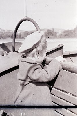 A young woman, likely a boat operator, steers a vessel with a visible wheel and nautical controls. She wears a beret and a lo...