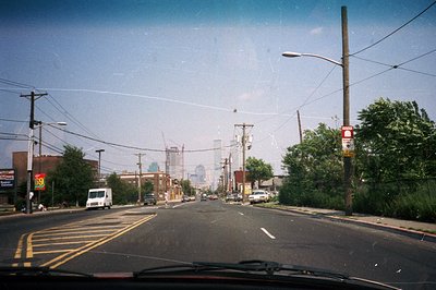 Urban street scene, likely USA, showcasing a two-lane road receding towards a hazy skyline. Telephone poles, overhead wires, ...