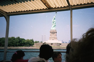 View of the Statue of Liberty framed by a boat's metal roof. The iconic landmark stands on a pedestal, with the Manhattan sky...