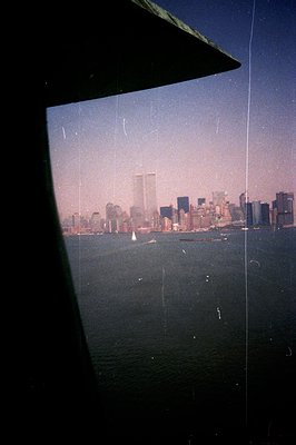 Framed view of the New York City skyline, featuring the World Trade Center towers prominently visible. The image shows a hazy...