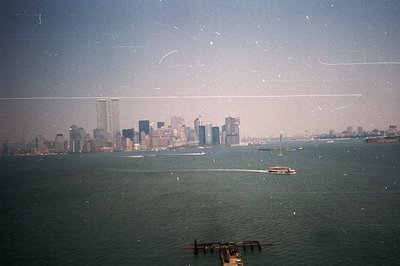A wide shot captures the New York City skyline across a body of water, likely the Hudson River. The iconic Twin Towers domina...