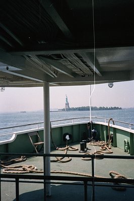 View from a ferry deck showcasing the Statue of Liberty rising from the Atlantic. The ship’s railings, ropes, and structure a...