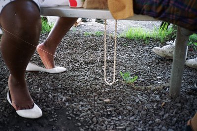 Close-up, gravel ground features a looping rope, suggesting a game or playful activity. A person in white flats and another w...