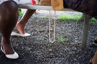 Close-up, slightly grainy image shows a person's feet in white ballet flats standing on a gravel surface. A rope loop hangs f...