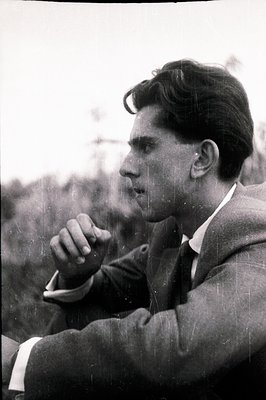 A young man in a suit, viewed in profile, rests his chin on folded hands. The image exhibits visible grain and surface scratc...