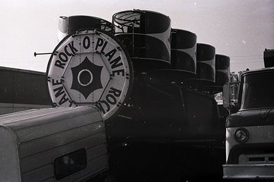Vintage semi-trucks lined up with "Rock-O-Plane Rock" branding on cylindrical fuel tanks, likely 1960s–1970s. Bold typography...
