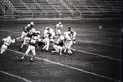 Intense mid-play action shot of an American football game, likely mid-20th century. Players in vintage helmets and jerseys cl...