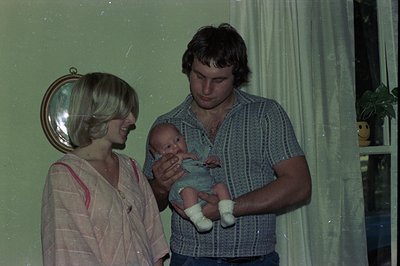 A 1970s indoor family portrait: woman in a light-colored blouse with red trim holds a vintage hair dryer, while a man in a st...