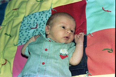 Vintage baby portrait on a colorful patchwork blanket, featuring a floral/butterfly-themed shirt. Soft focus and warm tones s...