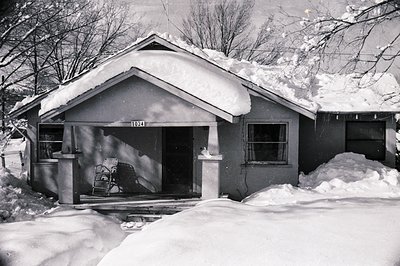 Mid-century single-story ranch-style home blanketed in snow, featuring a gabled roof and numbered facade (1024). Snow-covered...
